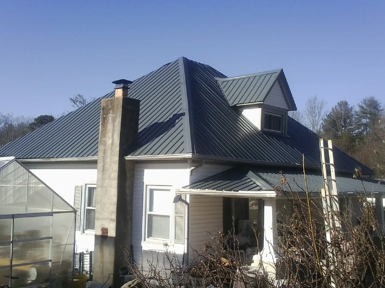 Dark blue standing seam metal roof on a white farmhouse with dormer — Slate & Tile Roof Repair by Roofing Brothers in Alledonia
