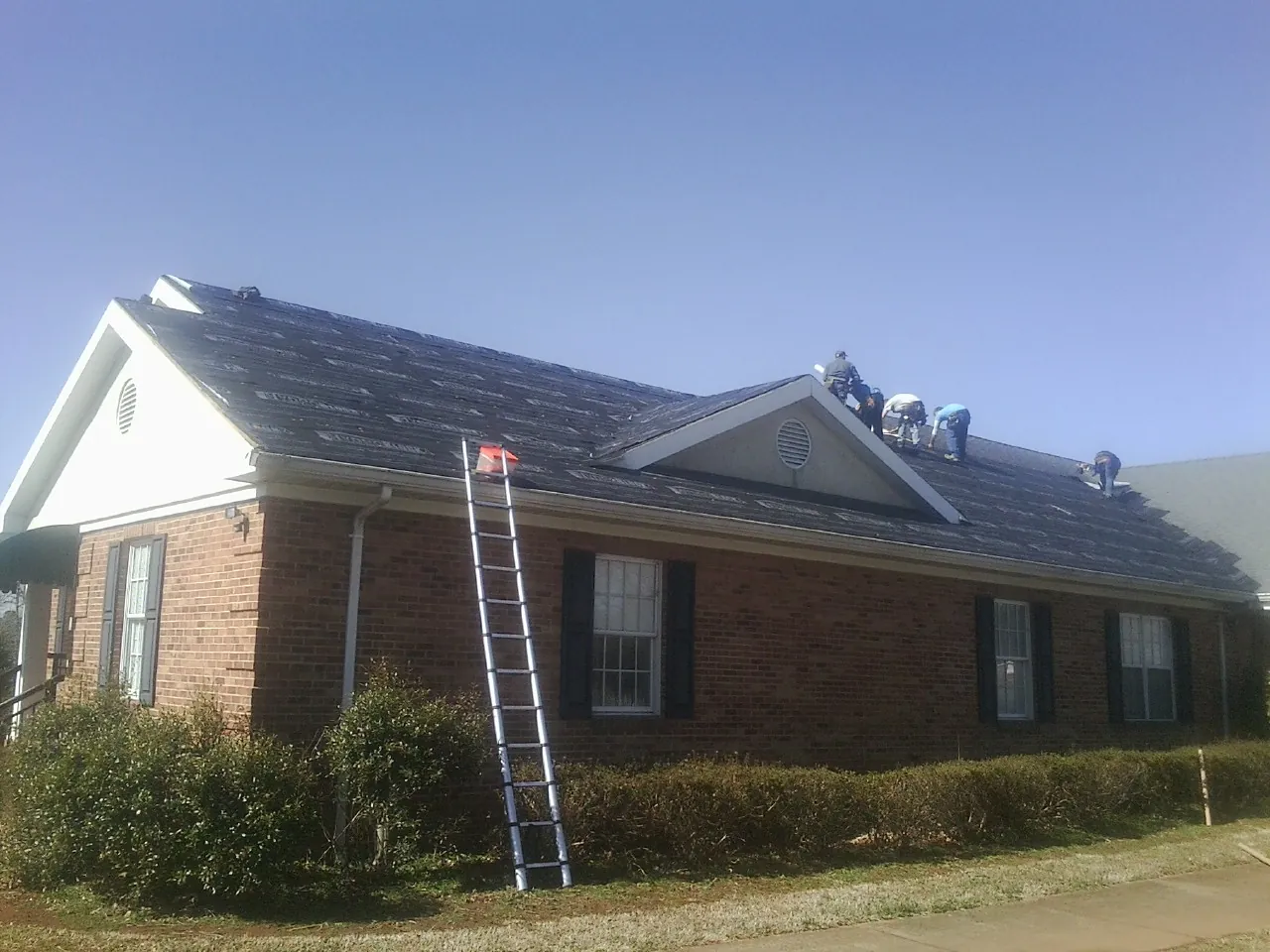 Crew tearing shingles off a brick ranch roof with a ladder set — Emergency Roof Repair work by our crew in Alledonia