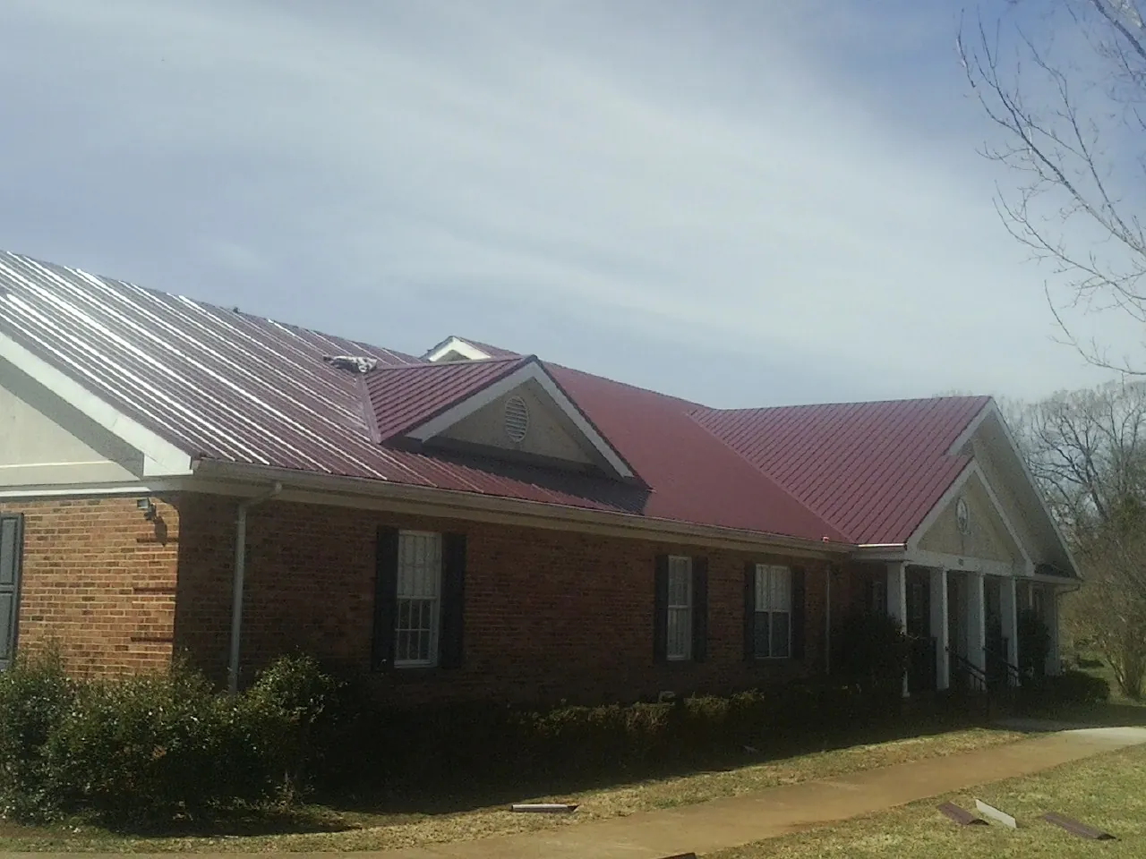Red metal roof with gabled entries on a long brick building, from a Hail Damage Roof Repair job in Alledonia