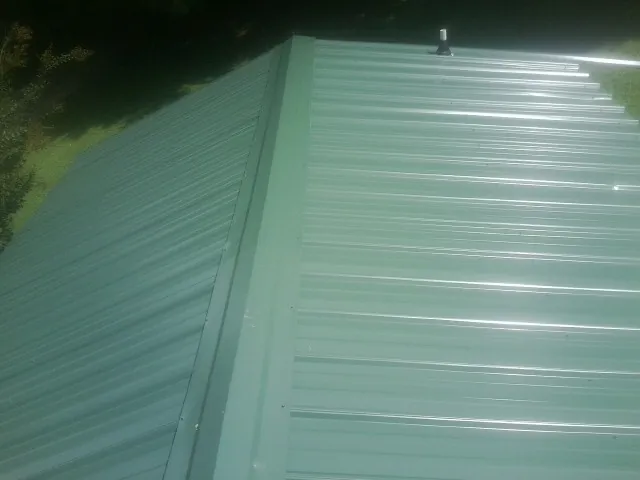 New green metal panels meeting at the ridge of a roof — Flat Roof Repair work by our crew in Alledonia