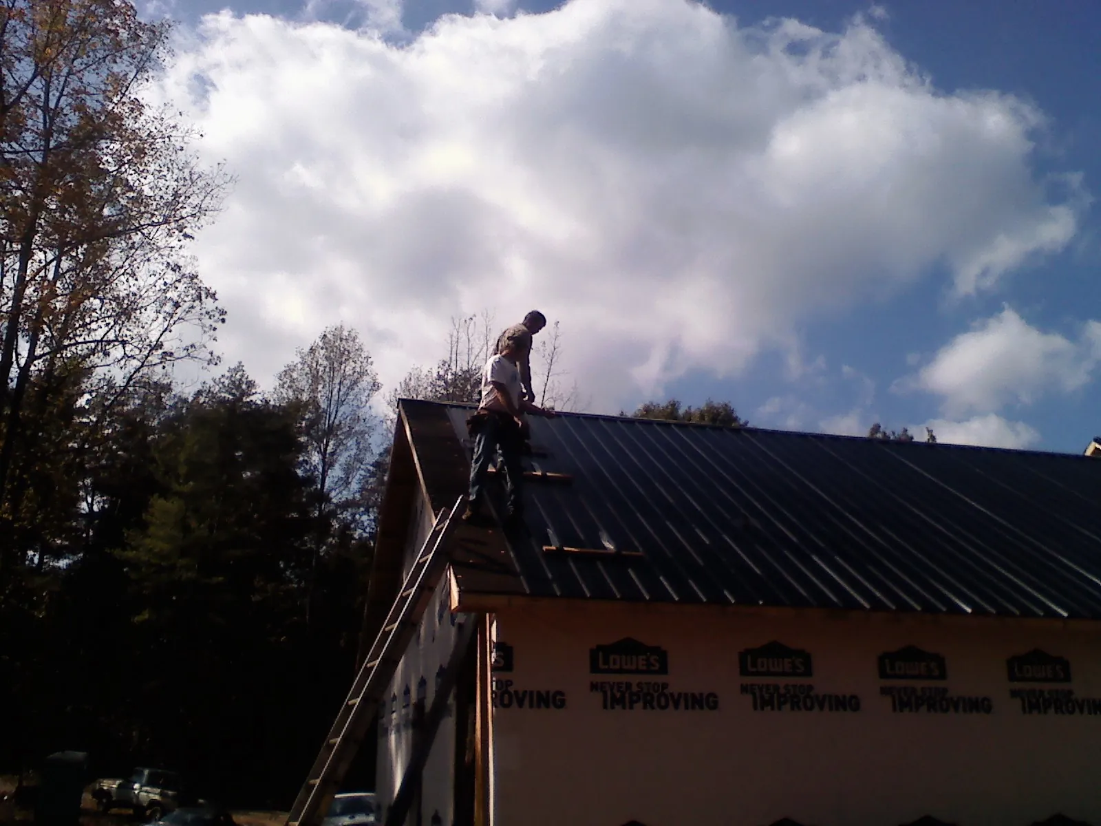 Roofer fastening dark metal panels high against a cloudy sky, from a Roof Inspection job in Alledonia