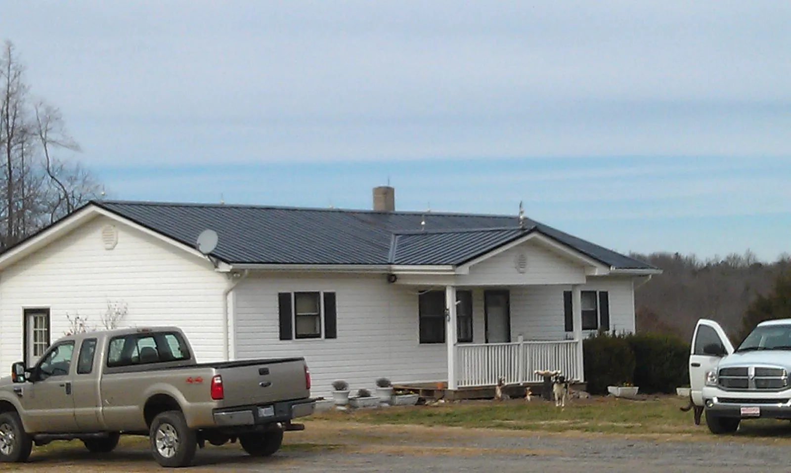 Finished dark metal roof on a white ranch home with work trucks parked in Alledonia