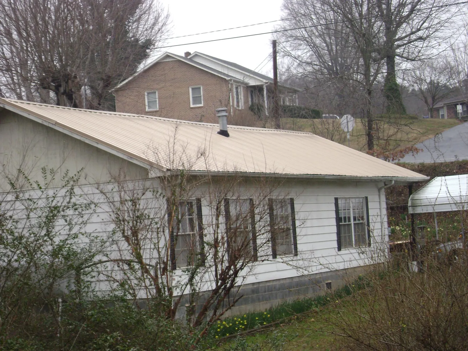 Tan metal roof on a white sided house set into a hillside — Commercial Roofing by Roofing Brothers in Alledonia