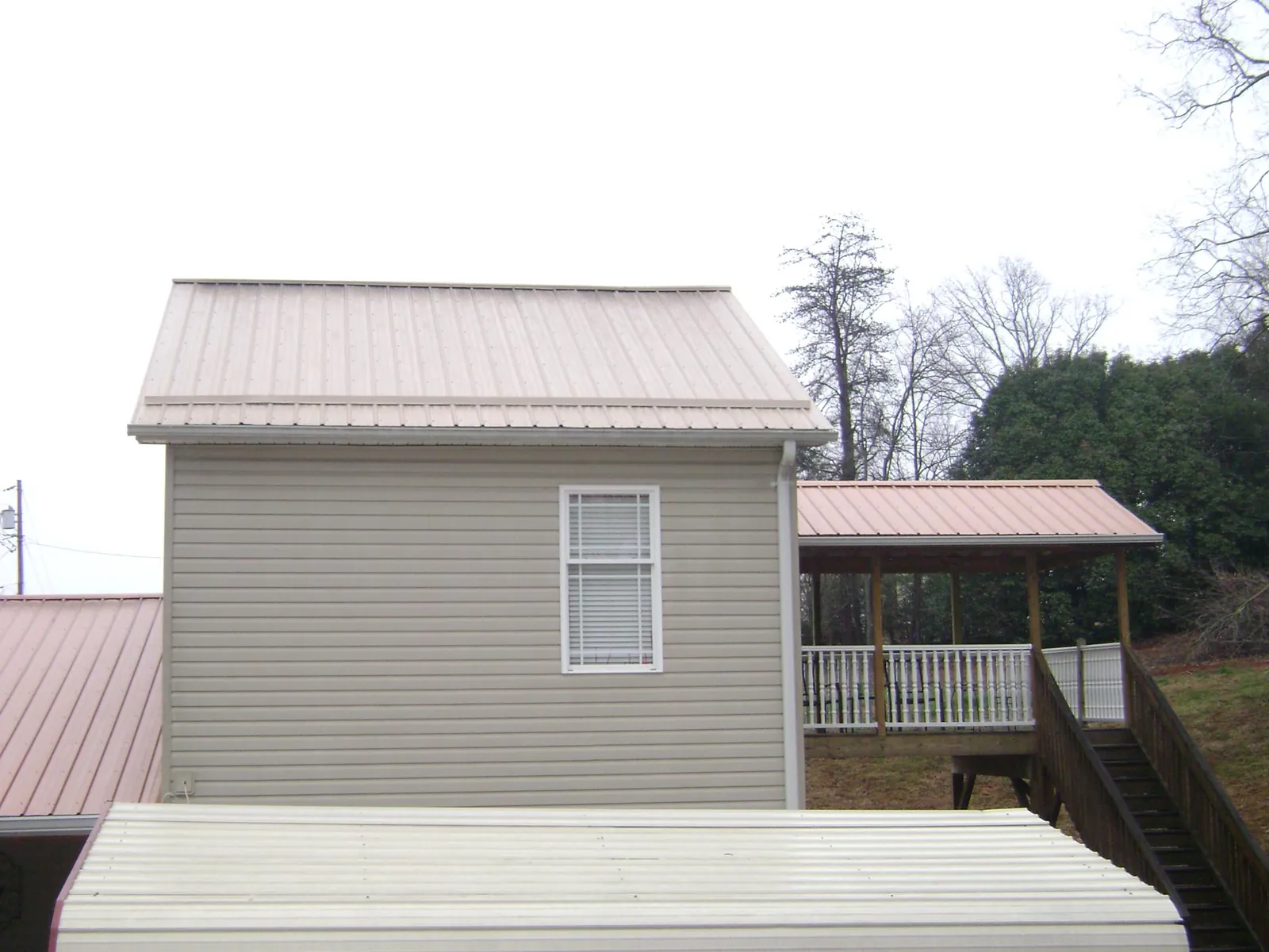 Tan metal roofs on a two story addition and attached porch, from a Roof Replacement job in Alledonia